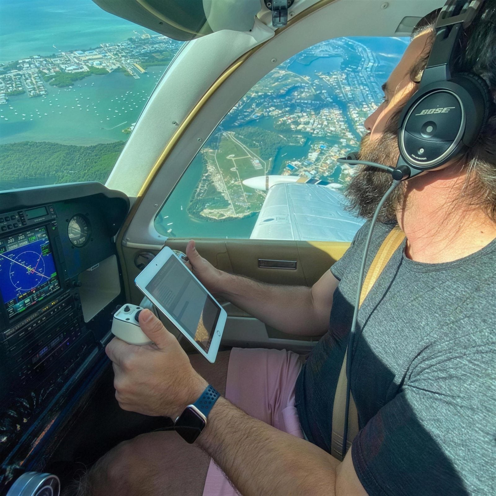 At the controls of a light aircraft, turquoise coastline through the windscreen.