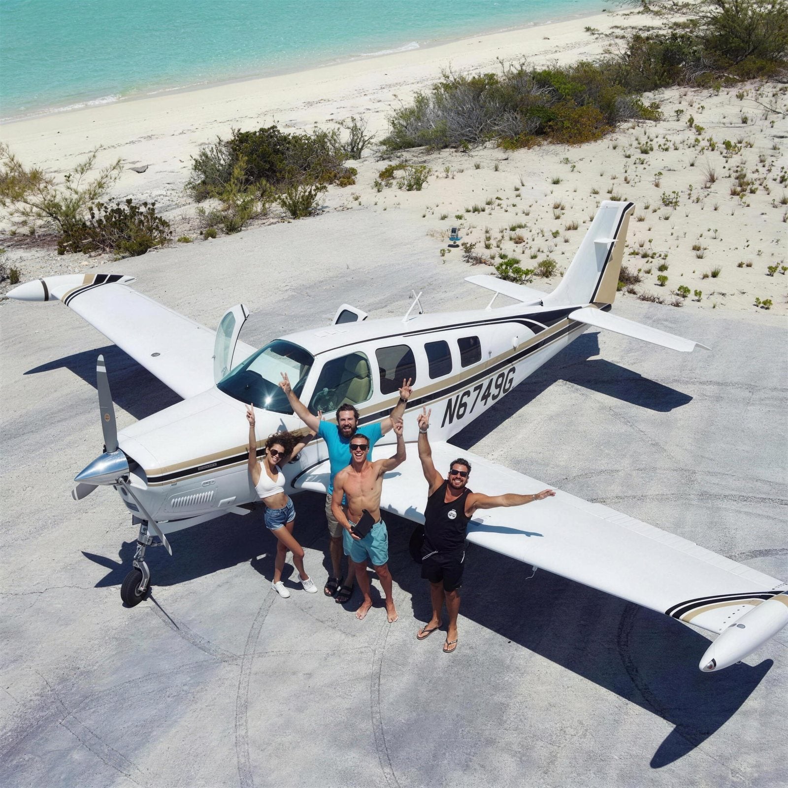 Four friends under the wing of a light aircraft parked on a beach airstrip.